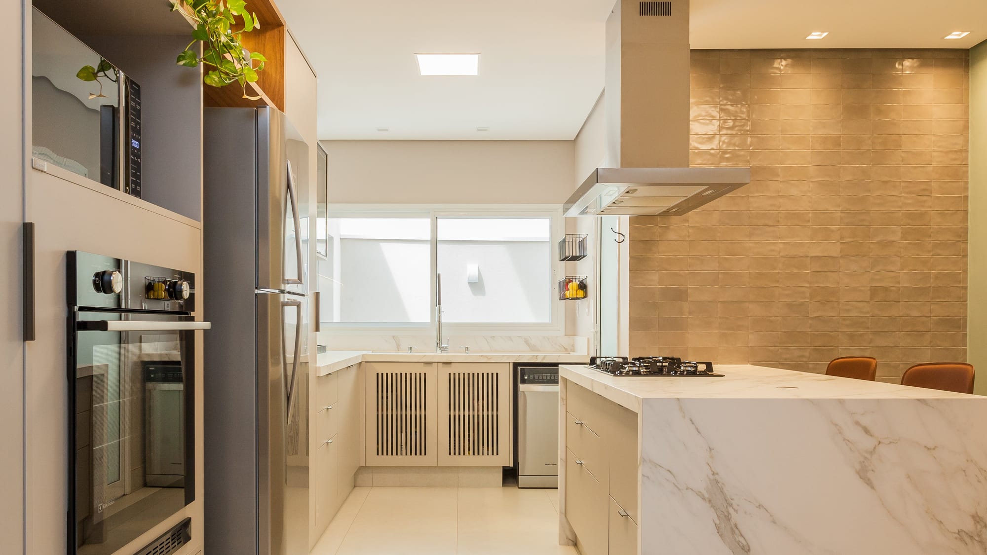 Cozinha reformada com marcenaria clara, bancada de mármore e parede em revestimento dourado
